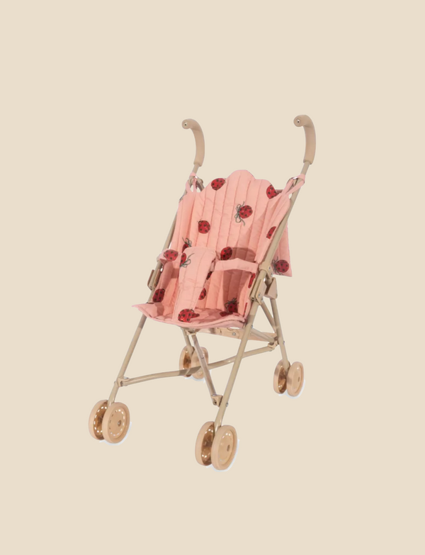 The Konges Sloejd Doll Stroller - Ladybug is a lightweight pink umbrella stroller with a playful ladybug pattern, designed for extra stability. It includes curved handles and four small wheels, all set against a solid beige background.