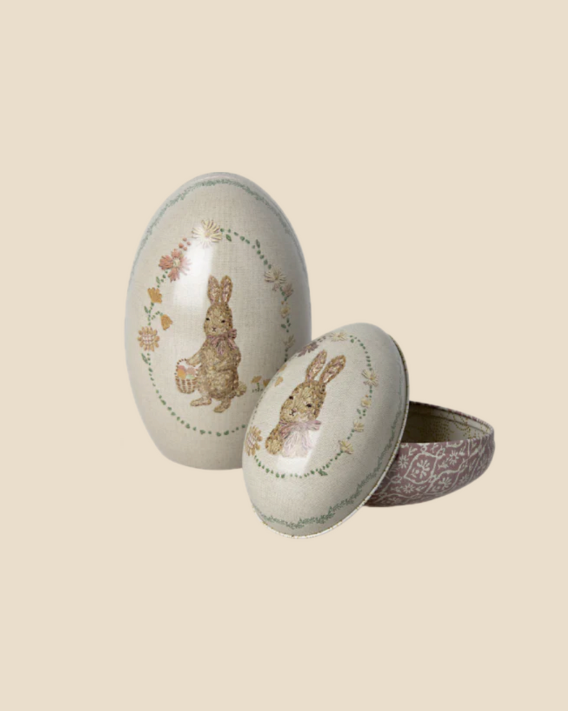 A set of two Maileg Easter Eggs, featuring metal construction with rabbit and flower illustrations. One egg is open, displaying a Dorthe Mailil embroidery-inspired pattern inside. These charming decorative pieces ship in approximately one week.