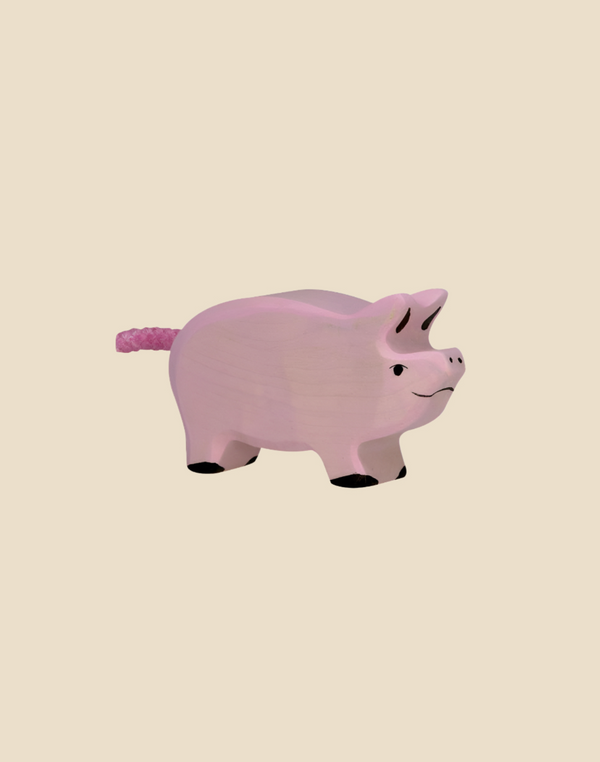 The Holztiger Piglet is a handcrafted wooden toy painted light pink with watercolors, featuring black hooves, a smiling face, and a textured pink tail. Ships in one week.
