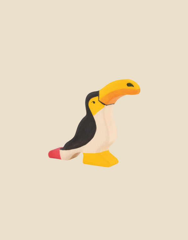 The Holztiger Toucan, handcrafted from maple and beech wood with a yellow beak, black back, white chest, and red tail, stands on a plain light beige background. Ships in one week.