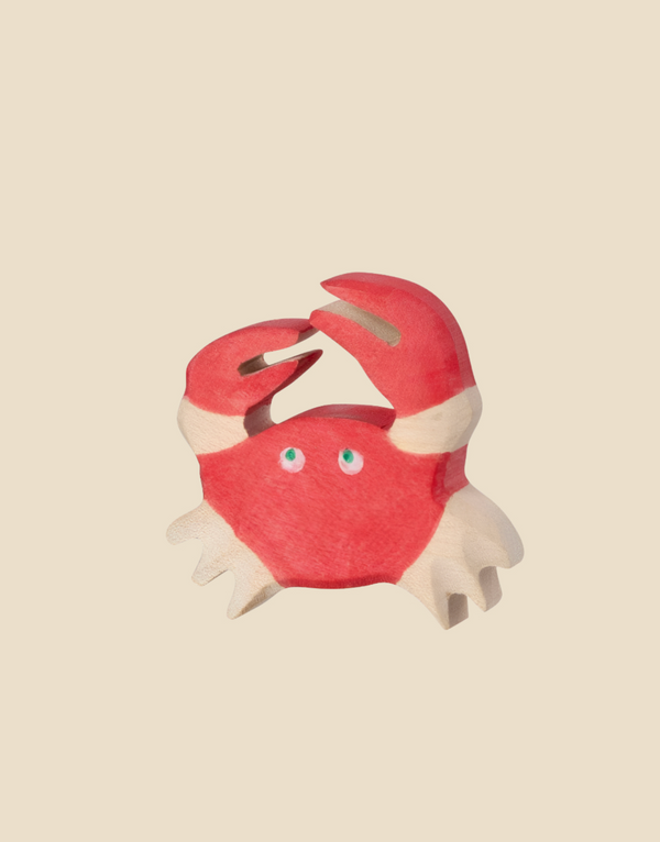 The Holztiger Crab, a red and white wooden cartoon crab with blue eyes, raises its claws against a beige background. Ships in one week.