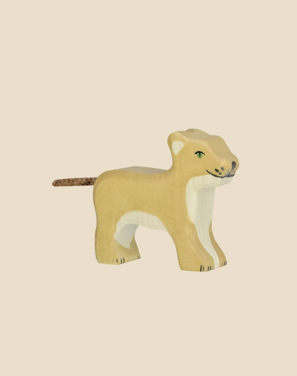 A handcrafted wood Holztiger Lion Cub, featuring a beige body with white accents and green eyes, stands on a light tan background. Made in Europe for quality and charm; ships in one week.