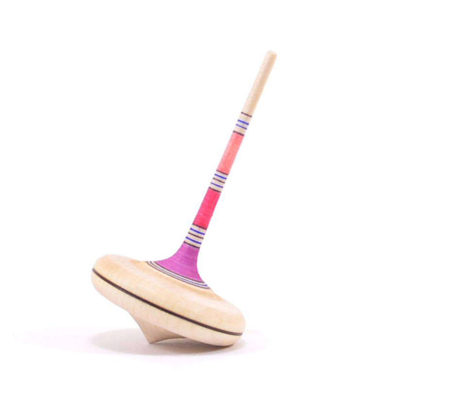 The Mader Spaghetti Spinning Top - Pink, made from maple wood with pink, purple, and blue stripes and a long handle, stands upright on a white background.