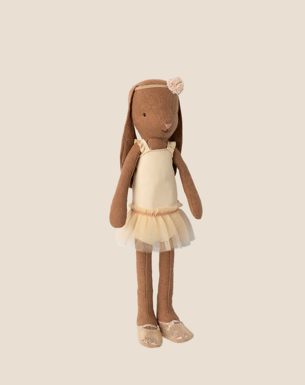 The Maileg Bunny, Size 2 in chocolate brown, wears a cream ballet suit and skirt, matching shoes, and a flower headband, standing upright against a light beige background.