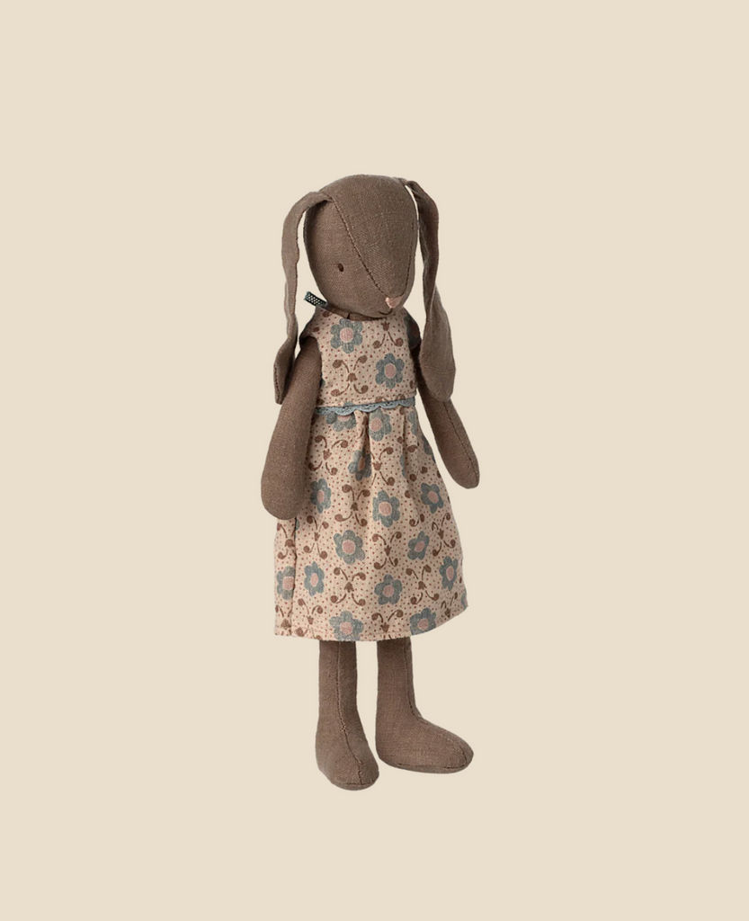 The Maileg Bunny, Size 2 - Brown - Dress, featuring floppy ears and a beige floral dress with blue and brown flowers, stands upright against a plain light beige background.