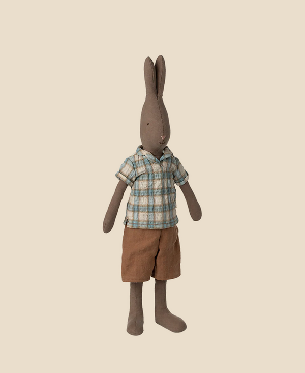 The Maileg Rabbit, Size 3 - Brown, is dressed in a plaid shirt and brown shorts, standing upright against a beige background, highlighting its charming outfit made from soft natural fabrics.