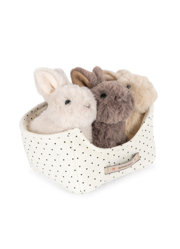The Konges Sloejd Bunnys in Basket Set includes a fabric basket with black polka dots, a front label, and four plush toy bunnies in cream, beige, brown, and gray resting on a cozy padded bed.