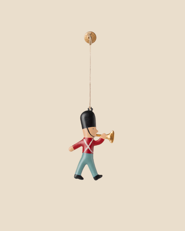 The Maileg Metal Ornament, Guard - Trumpet features a marching toy soldier in a red coat and blue pants playing a golden trumpet—a charming holiday decoration for your Christmas tree.