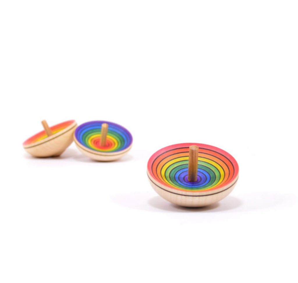 The Mader UFO Spinning Top - Purple Rainbow, crafted from maple wood, displays vibrant rainbow concentric circles and is pictured on a white background with one in focus and two slightly blurred behind.