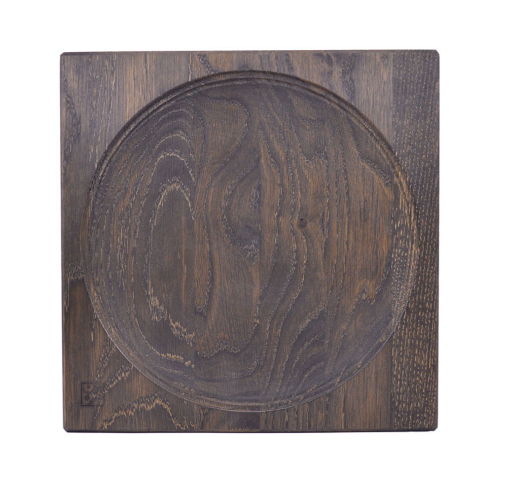 The Mader Black Oak Spinning Plate features a square black oak design with a circular indented center, visible dark wood grain, a small engraved logo, and is crafted to meet toy safety standards.