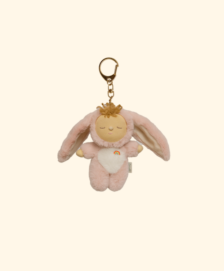 The Olli Ella Cozy Bag Charm - Bunny Flopsy is a soft pink bunny plush keychain with long floppy ears, closed eyes, a white heart on its chest, and a gold keyring—ideal as a cute bunny bag charm.
