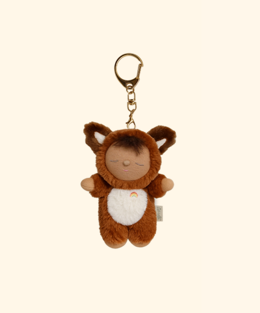 The Olli Ella Cozy Bag Charm - Fox Finnley features a small, brown plush doll in a fox costume with closed eyes and a rainbow on its white belly. This adorable keychain comes with a gold clasp and is perfect for accessorizing bags.