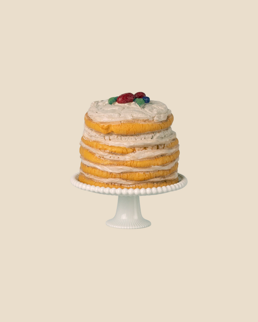 The Maileg Party Cake and Cake Stand, Mouse - Off White (available for pre-order; expected arrival by 05/01/26), features a layered sponge cake with white frosting, red and blue berries, and green leaves on a white stand against a beige backdrop.