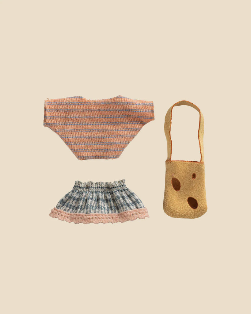 A flat lay of doll clothes—a pink and blue striped knit top, a blue plaid skirt with a pink lace hem, and a yellow shoulder bag—perfect for dressing up your Maileg Little Sister Mini House Set.