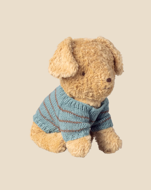 A plush puppy with floppy ears wears the Maileg Knitted Puppy Sweater in dusty blue with brown stripes, shown against a beige background. Available for pre-order; expected arrival by 04/15/26.