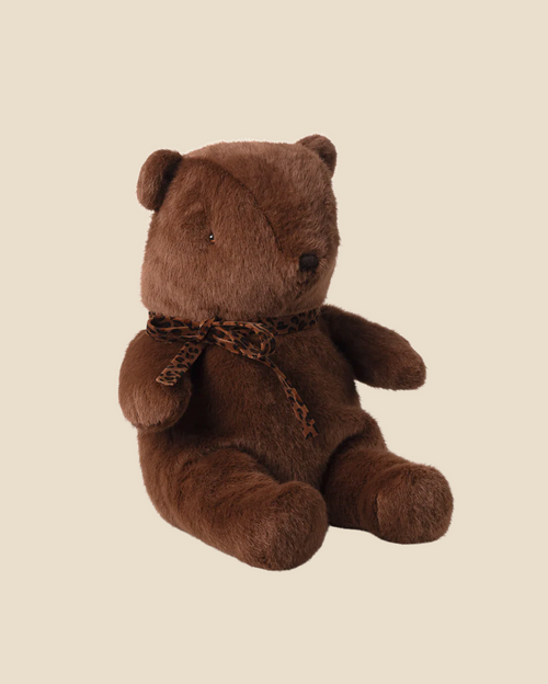 The Pre-order: Maileg Teddy Bear Plush, Medium - Dark Chocolate sits upright against a plain beige background, featuring a soft plush exterior and a leopard print ribbon tied around its neck. Expected arrival by 06/15/26.