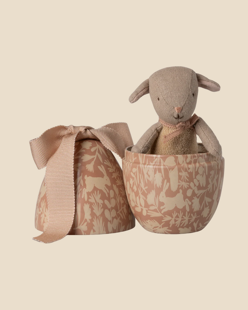 The Pre-order Maileg Easter Egg with Micro Lamb, Small - Powder features a tiny plush lamb inside a floral-patterned metal egg container, accompanied by a matching lid adorned with a textured ribbon bow.