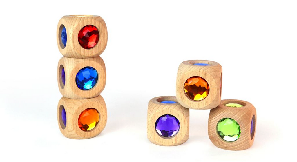 Five Bauspiel Magic Cube (Single) wooden blocks, each with a colorful faceted gem—red, orange, blue, purple, and green—are shown. Three blocks are stacked on the left; two stand alone on the right.