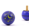 The Mader Luna Turn-Over Spinning Top, featuring a starry sky design with yellow stars and crescent moons, rests on a white surface; one top stands upright while another lies on its side, displaying the celestial pattern.