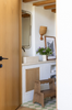 A cozy entryway with a wooden door, vintage mirror, small countertop displaying a framed photo, vase of flowers, woven wall basket, and the Margot Step Stool on a green-and-white checkered tile floor.