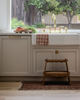 A cozy kitchen scene with a farmhouse sink, brass faucet, and a checkered dish towel. The Margot Step Stool sits on a patterned rug, while fresh vegetables are arranged on a cutting board by the window.
