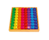 A wooden tray holds rows of Bauspiel Lucent Cylinders—round, colorful translucent tokens—arranged in a rainbow pattern with green, yellow, orange, red, pink, purple, and blue sections in neat lines.
