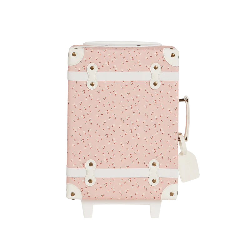 A pink suitcase with a floral pattern, featuring white straps and silver buckles, displayed against a black background. The handle is extended, ready for travel. This is the Olli Ella See-Ya Suitcase - Pink Daisies.