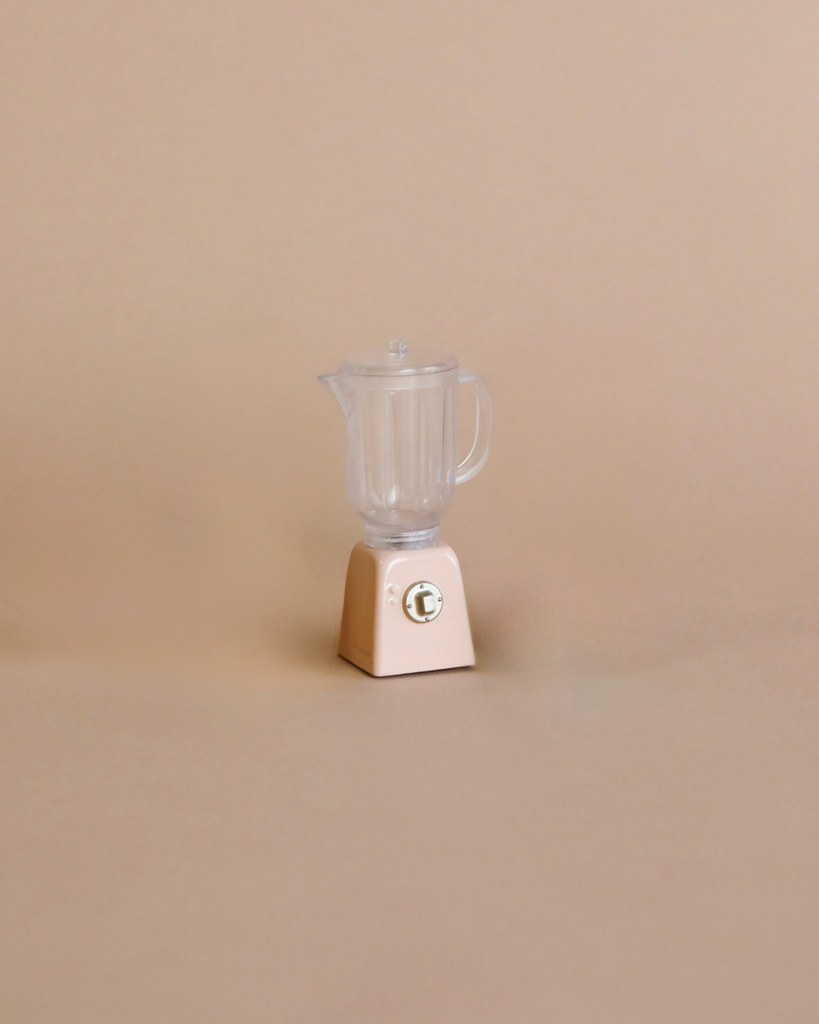 A small, beige blender with a clear container and lid sits on a light brown background. Ideal for dollhouse accessories or the Maileg Kitchen Set, this miniature blender perfectly complements your collection.