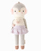 Cuddle + Kind Skylar The Penguin is a handmade knit cotton doll with gray and white coloring, pink earmuffs, a white scarf with pink accents, lavender skirt, taupe shoes, and pink cheeks—a charming fair trade plush toy.