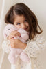 A young girl in a cream floral dress hugs her super soft Snuggle Bunnies - Frankie the Hugging Bunny - Blossom plush and smiles sweetly, tilting her head against a light, neutral background.