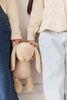 Two people wearing light sweaters and jeans stand side by side, cropped to show only their torsos and legs. One holds the Snuggle Bunnies - Penelope - Caramel plush bunny by its ear.