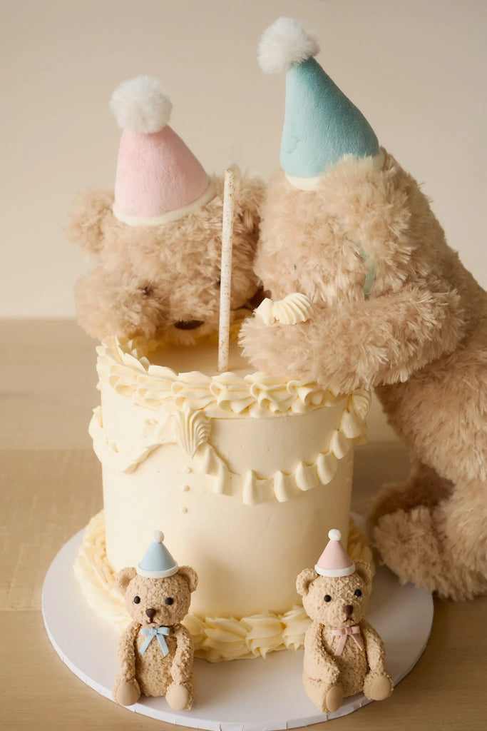 Two Snuggle Bunnies - Birthday Arthur - Sky plush toys in pastel party hats lean over a white-frosted cake, while two mini bunny cake toppers with bows and hats complete this festive keepsake gift scene.