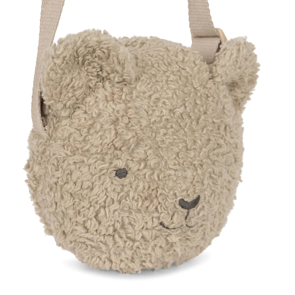 A plush Teddy Bear Shoulder Bag with an organic sherpa, curly beige surface, featuring stitched eyes and a smiling mouth, and an attached adjustable shoulder strap.