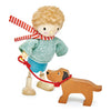 A toy figure with curly hair and a blue sweater, known as Mr. Goodwood and his Dog, standing beside a solid wood toy dog on a red leash, set against a white background.