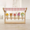 A solid wood toy Ice Cream Scoops and Smiles stand displaying six colorful ice cream cones with cute animal faces, set against a soft-focus interior background.