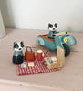 The Badger Picnic Motorbike Ride set features two wooden badger figurines with a blue motorbike and sidecar, enjoying a picnic playset on a red checkered cloth with cups, plates, and food on a light wooden surface.