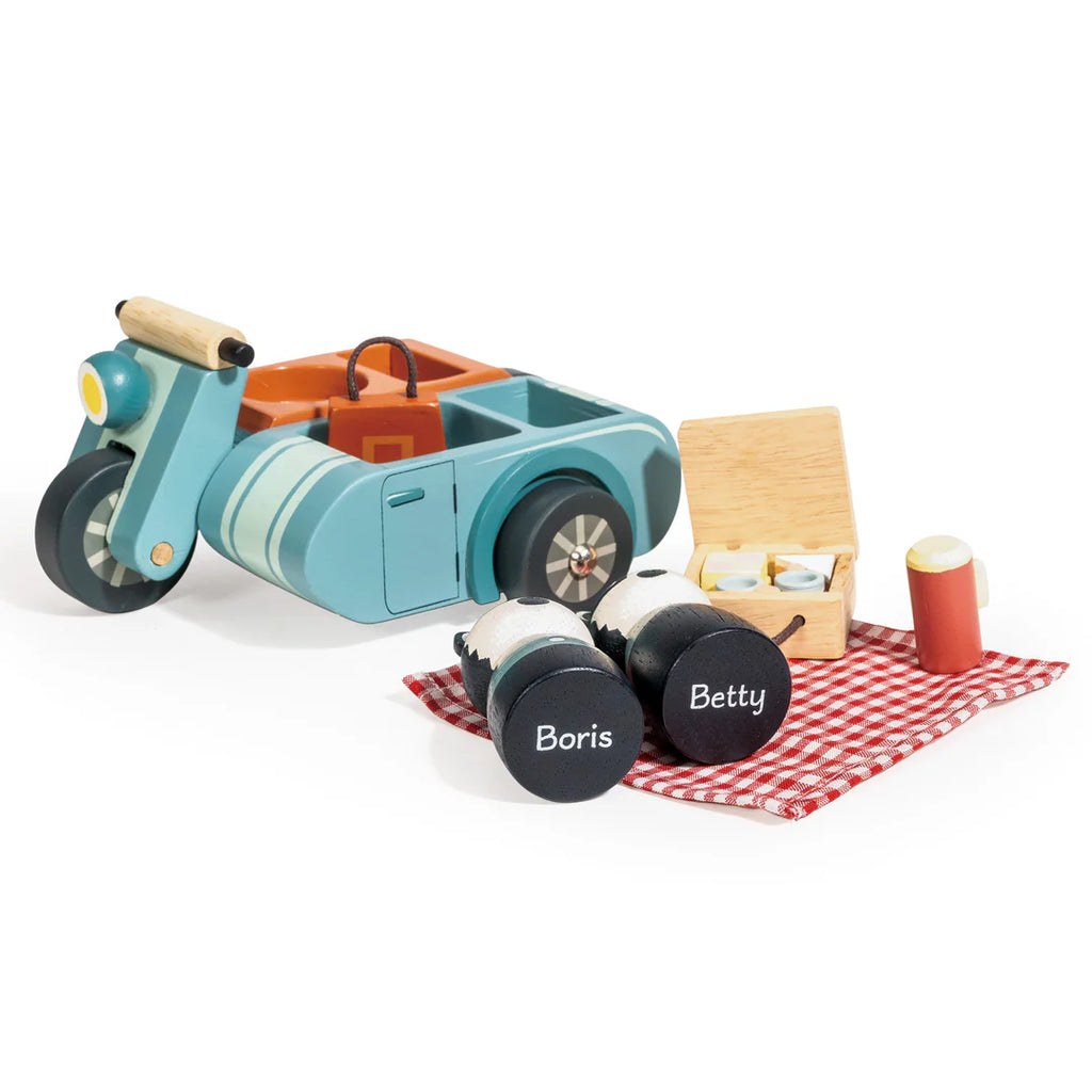 The Badger Picnic Motorbike Ride features a motorbike with sidecar, a red checkered picnic blanket, Boris and Betty plush toys, mugs, basket, and food accessories for kids to enjoy a fun pretend picnic adventure.