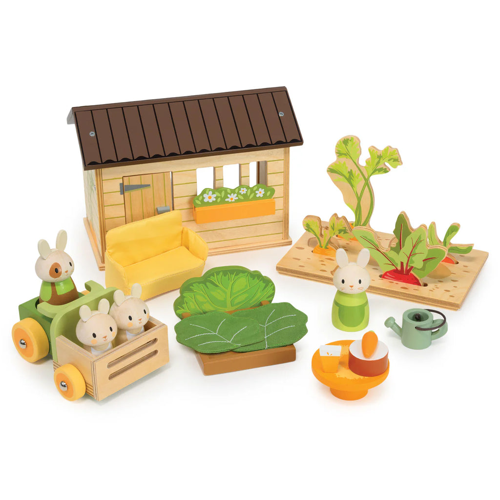Introducing Bunny’s Carrot Patch: a charming vegetable garden playset featuring bunny rabbit toy figures, a small wooden house reminiscent of a dollhouse, sofa, cart, leafy plants, watering can, and toy veggies—all thoughtfully arranged for imaginative play.