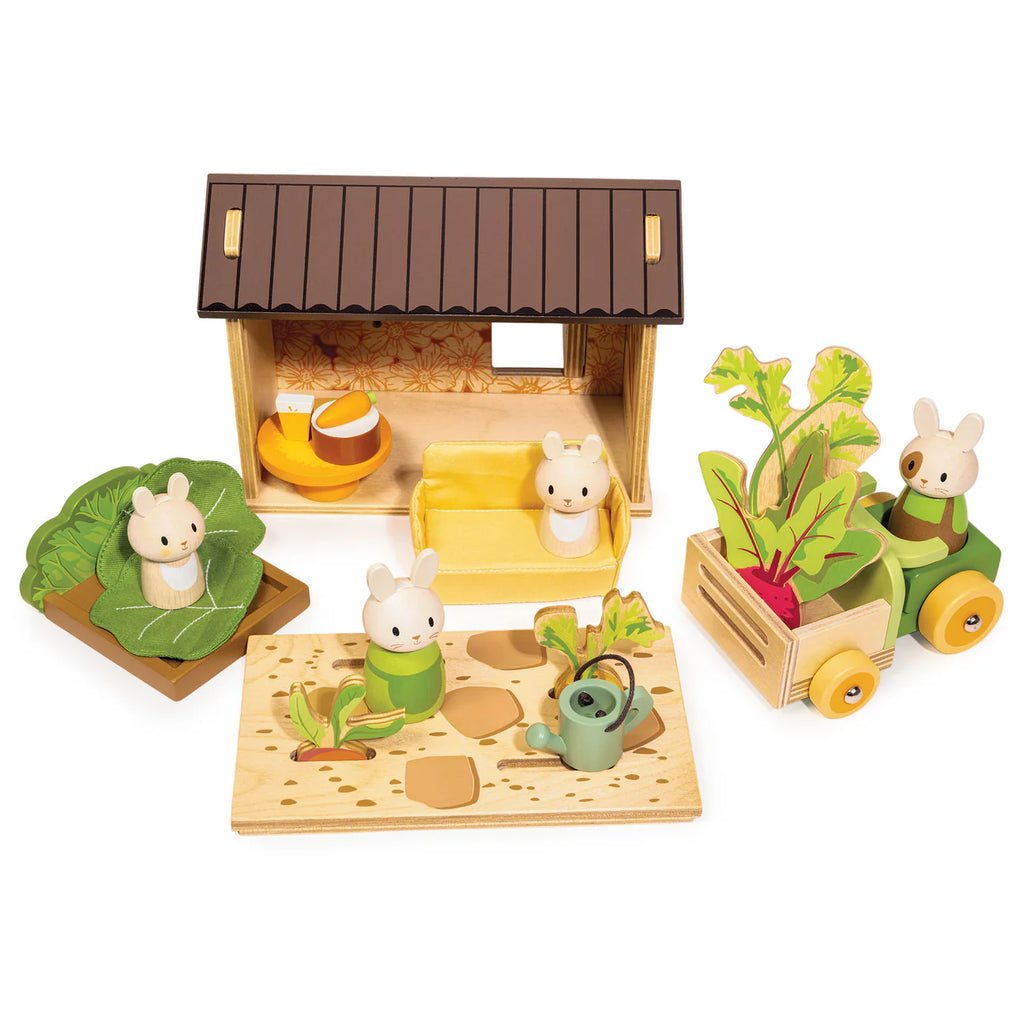 Bunny’s Carrot Patch is a wooden toy set that includes bunny figures, a charming wooden dollhouse, a vegetable garden playset with a crate of crops on a cart, a watering can, and other garden-themed accessories arranged for imaginative play.