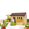 Introducing Bunny’s Carrot Patch, a charming wooden toy set featuring a bunny rabbit outside a small wooden dollhouse, surrounded by other bunnies, a toy tractor, and colorful vegetable garden playset accessories—all displayed on a clean white background.