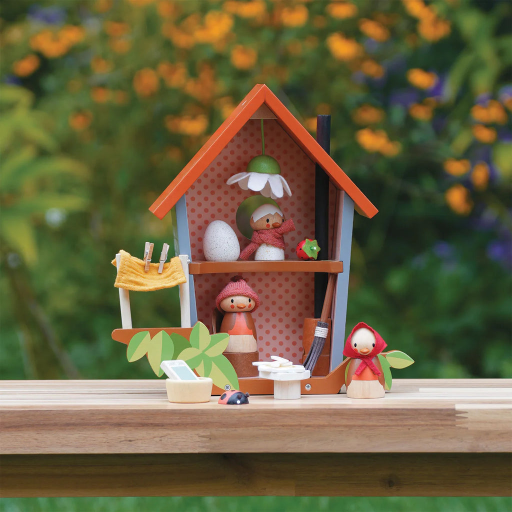 Robin's Nest Box is a charming wooden set featuring a red-roofed dollhouse, small wooden figures, a duck, and a clothesline with yellow shirt. Designed for imaginative play outdoors among greenery and flowers, it's an ideal storytelling toy.
