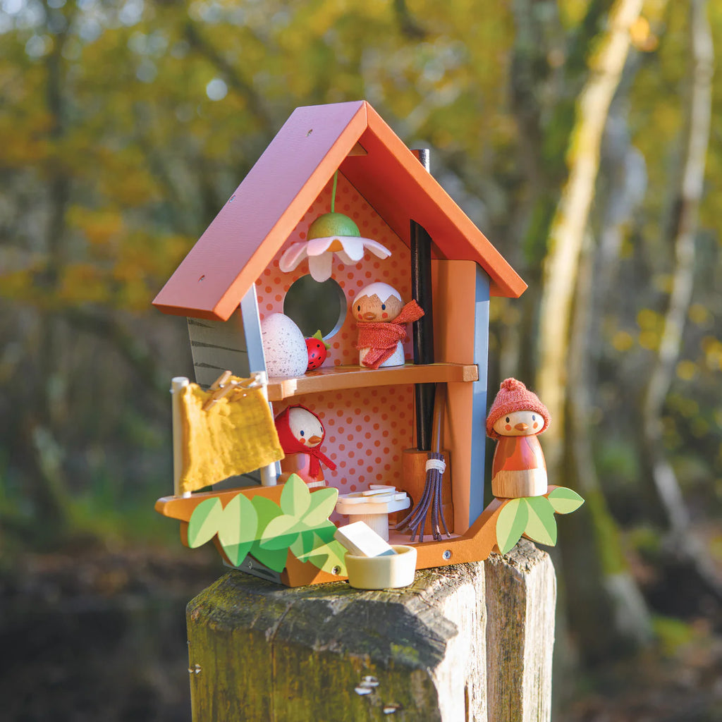 Robin's Nest Box rests on a tree stump outdoors, featuring small red-capped dolls, mini furniture, and autumn-inspired accents—an enchanting storytelling toy for imaginative play beneath sunlit trees.