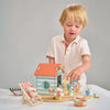 A young child engages in imaginative play with Sandy's Beach Hut and various wooden toys made of sustainable wood on a table, displaying curiosity and deep engagement.
