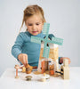 A young girl engages in imaginative play with a Penny Windmill toy set, including animals and other elements on a table, focusing intently on placing a piece.