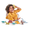 A joyful toddler with curly hair, wearing a yellow shirt, plays with the Dinosaurs Set on a white background, lifting one dinosaur above their head.