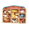 A wooden toy shelf displaying the Farmyard Animals Set, which includes assorted animal figures like cows, pigs, sheep, chickens, and a tractor, all made from sustainably sourced rubberwood, set against a plain.