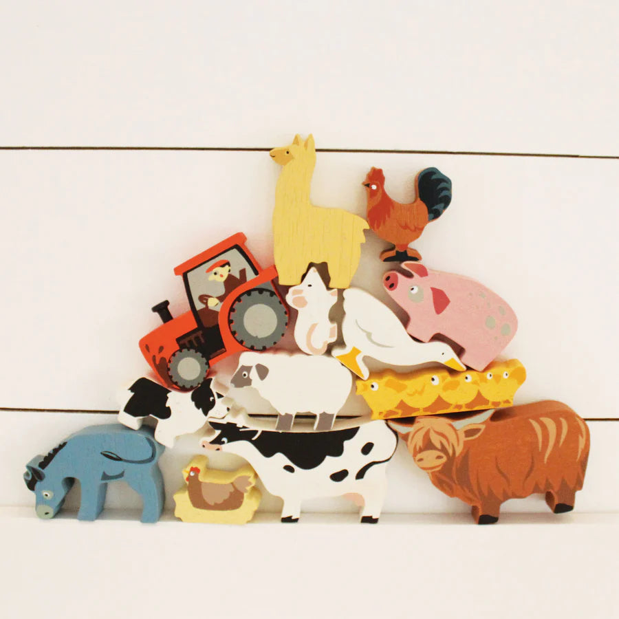 Sentence with Product Name: A colorful stack of Farmyard Animals Set, including a cow, pig, hen, tractor, and more, made from sustainably sourced rubberwood, arranged against a white wooden background.