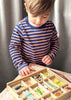 A young child in a striped shirt playing with The Bug Hotel toy puzzle with animal shapes at a table. The focus is on the child's engagement with the puzzle.