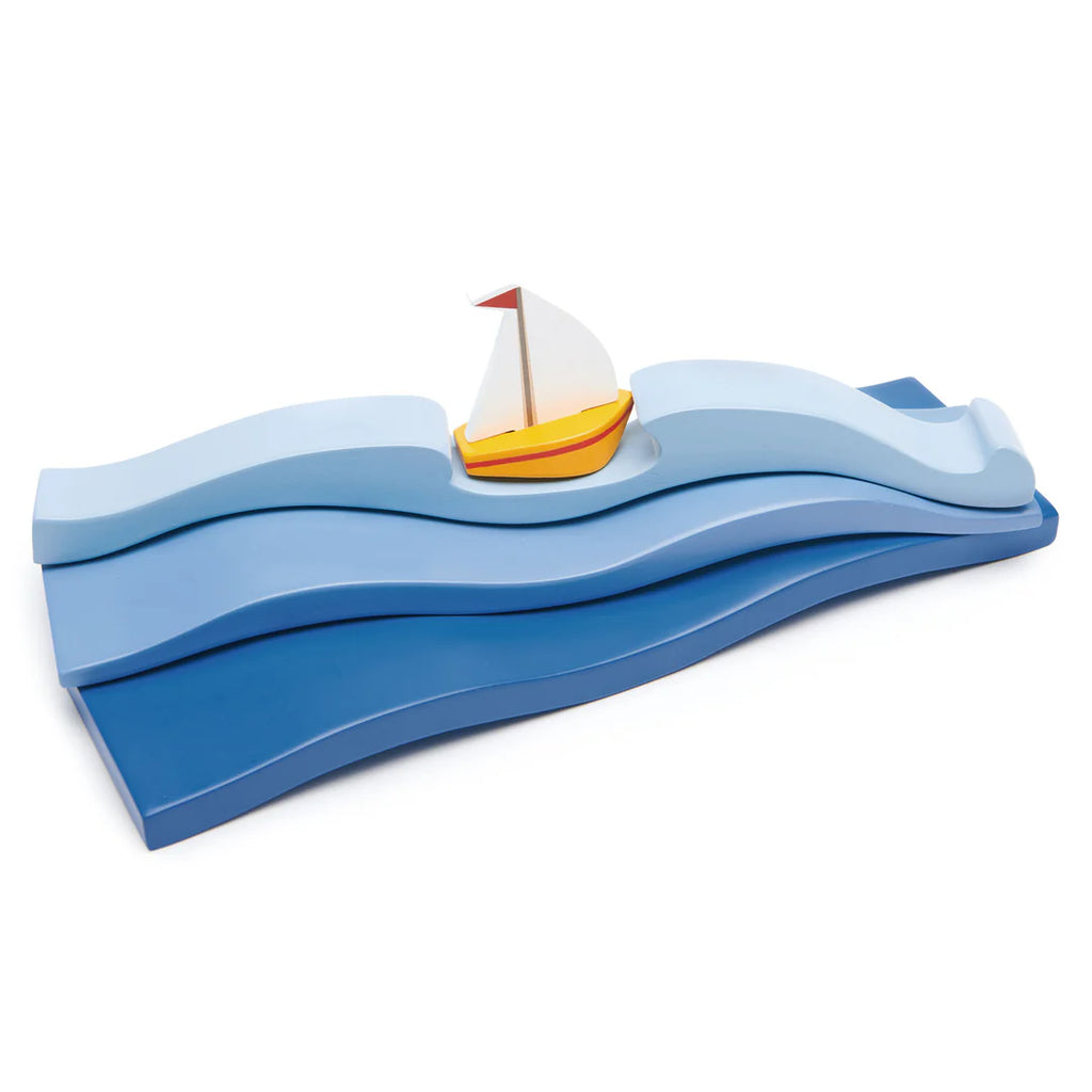 A Blue Water and Sail Boat Set with a white sail and yellow hull sits atop layered, wavy blue solid wood blocks representing waves of water. The blocks create a gradient of blue shades, indicating depth and movement, making it perfect for open-ended play. The scene is simple and stylized.