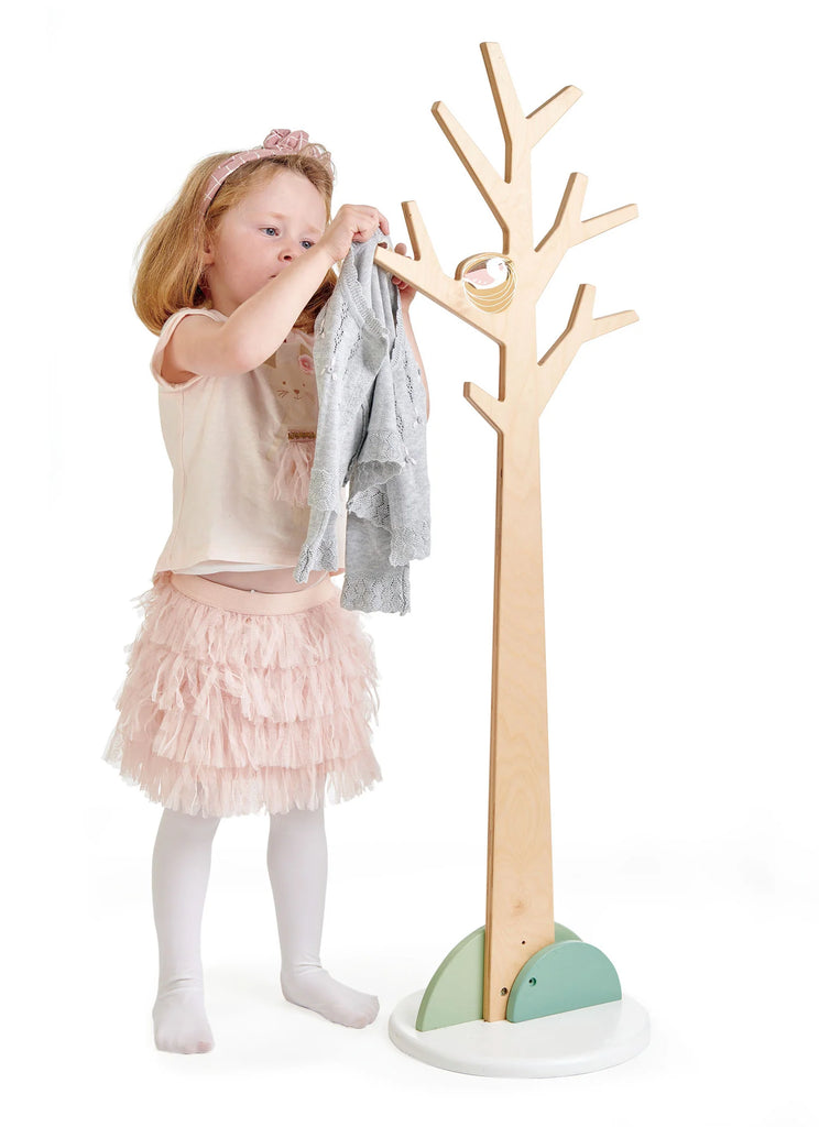 A young girl wearing a pink skirt and tiara hangs clothes on a stylish Forest Coat Stand against a white background.